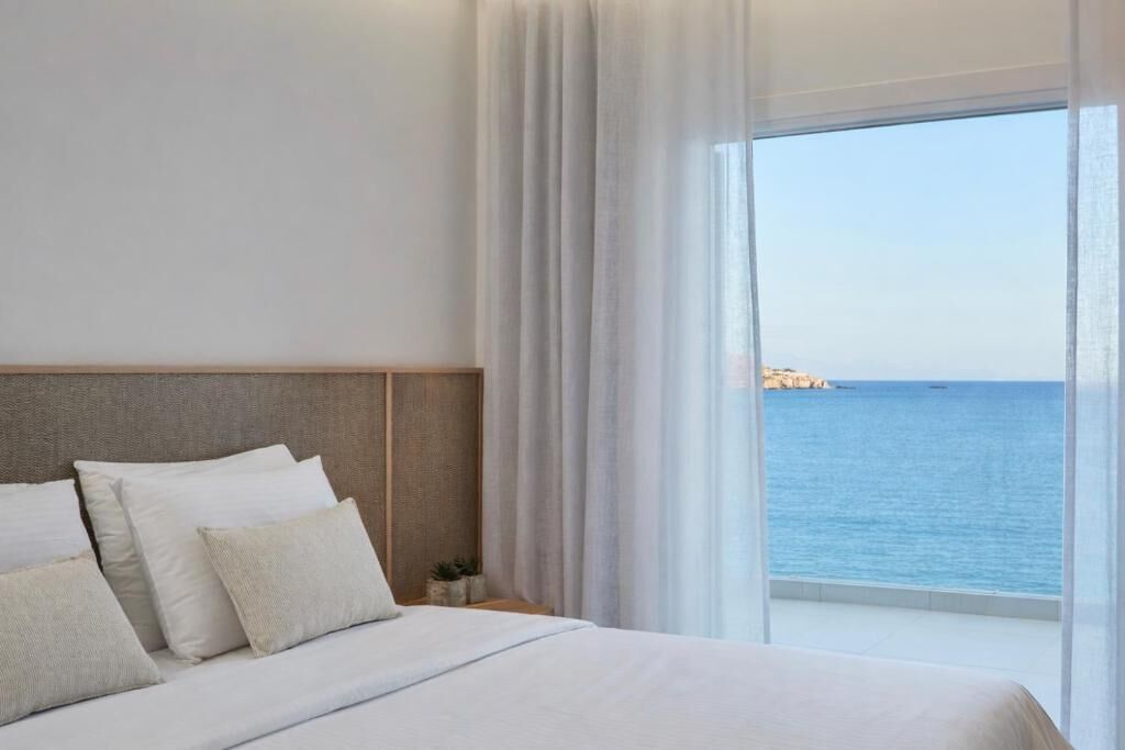 Habitación de hotel con una cama grande, cabecera y vista al mar.