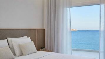Habitación de hotel con una cama grande, cabecera y vista al mar.