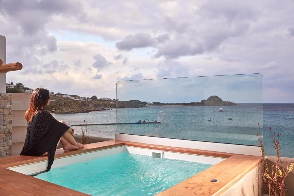 Una persona sentada junto a una piscina con vista al mar y a los barcos.
