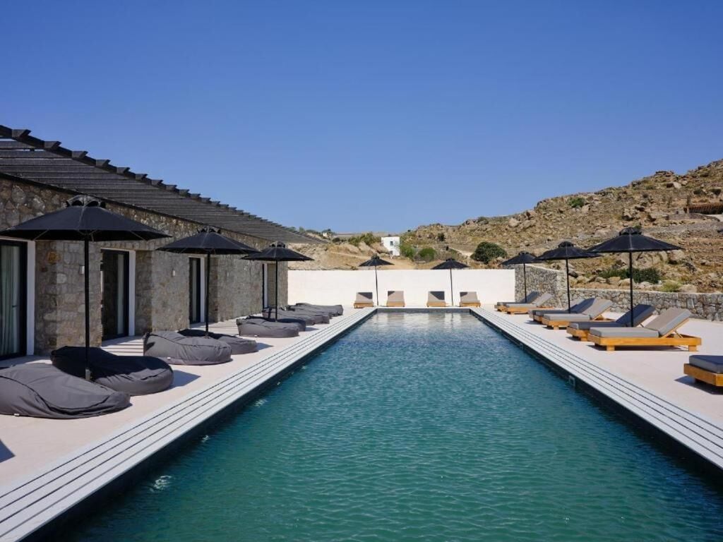 A swimming pool with lounge chairs and umbrellas, surrounded by stone walls and a clear sky.