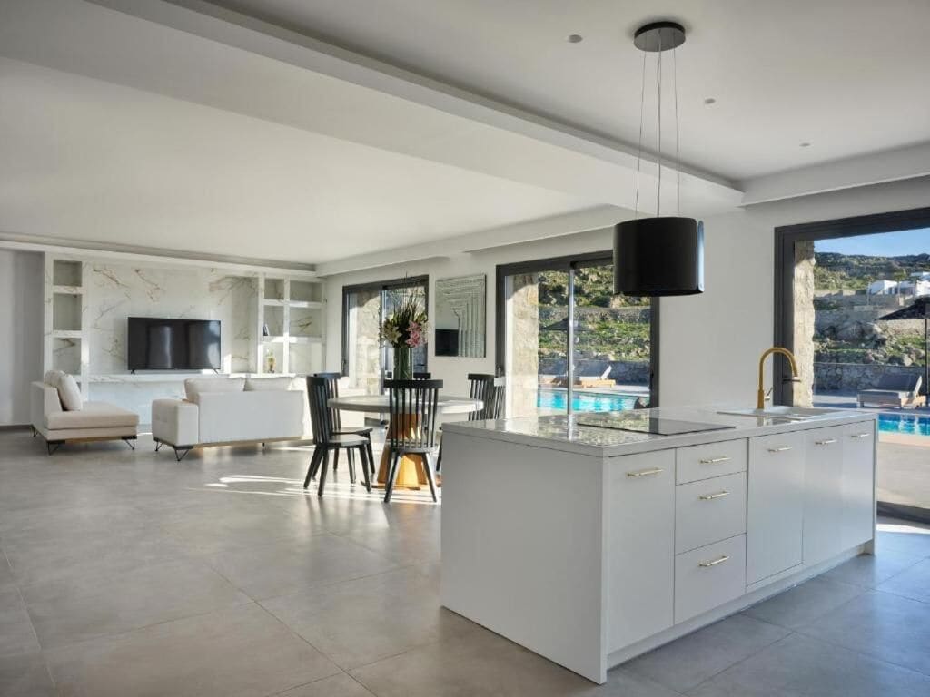 A spacious living area with a large island kitchen, a dining table, and a view of a swimming pool.