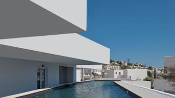 Un edificio moderno con piscina, paredes exteriores blancas y un cielo azul despejado.