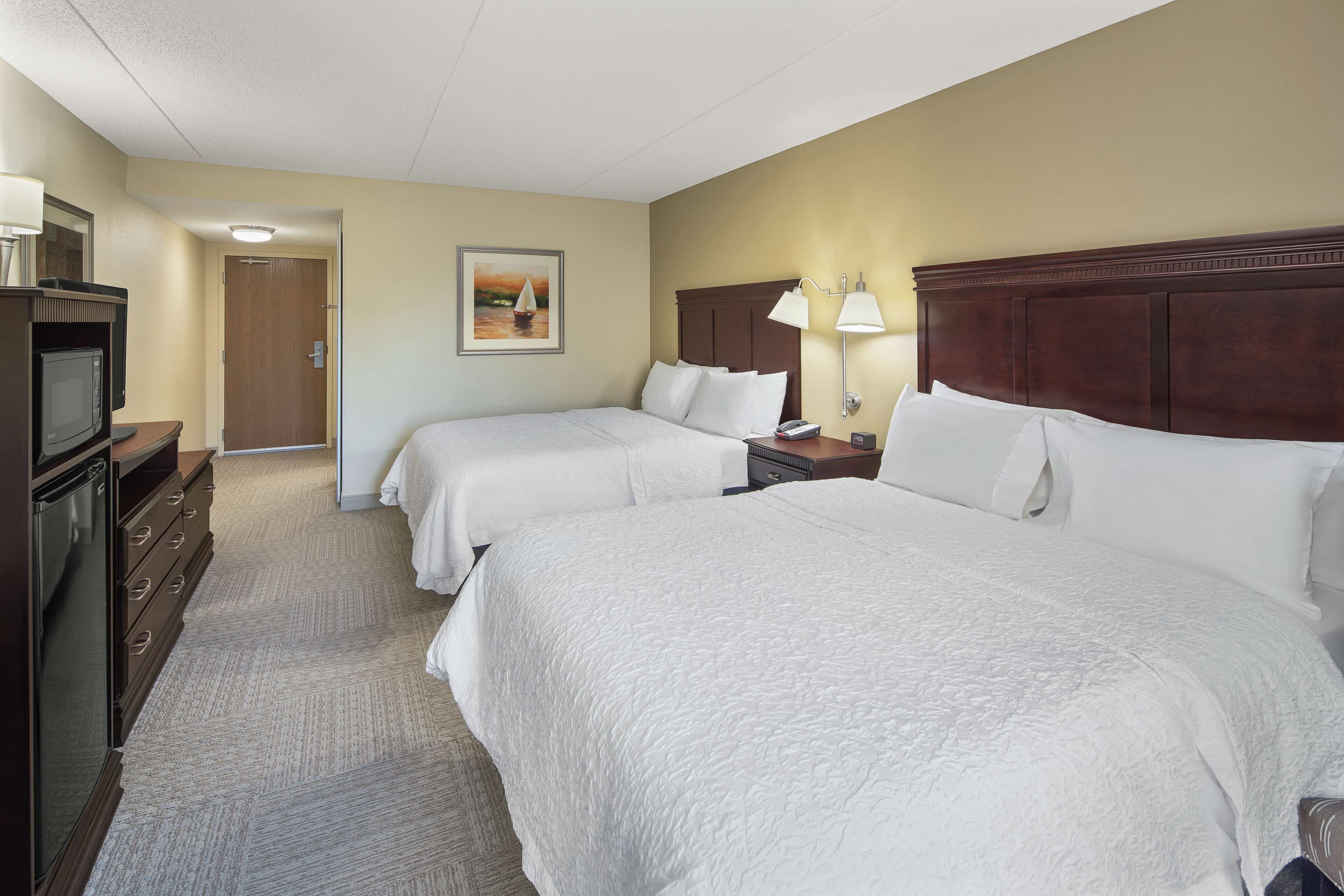 A hotel room with two beds, a television, a desk with a lamp, and a painting on the wall.