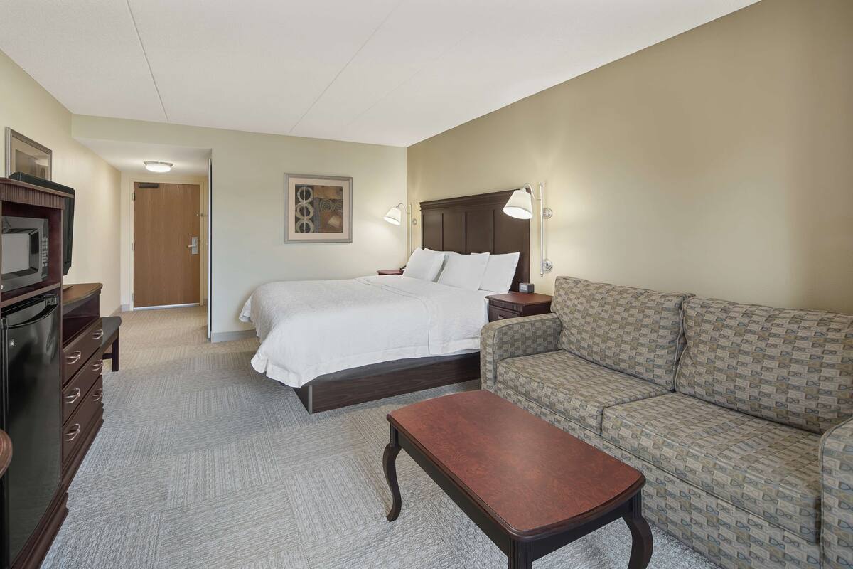 A hotel room with a bed, a sofa, a desk, and a television.