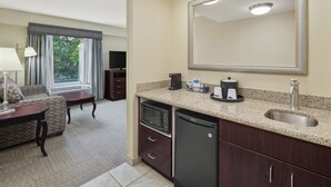 A compact hotel room with a kitchenette, a large mirror, a sofa, a dining table, and a view of the outdoors.