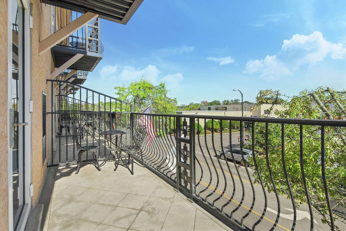 A balcony with outdoor furniture, a view of the street, and a clear sky.