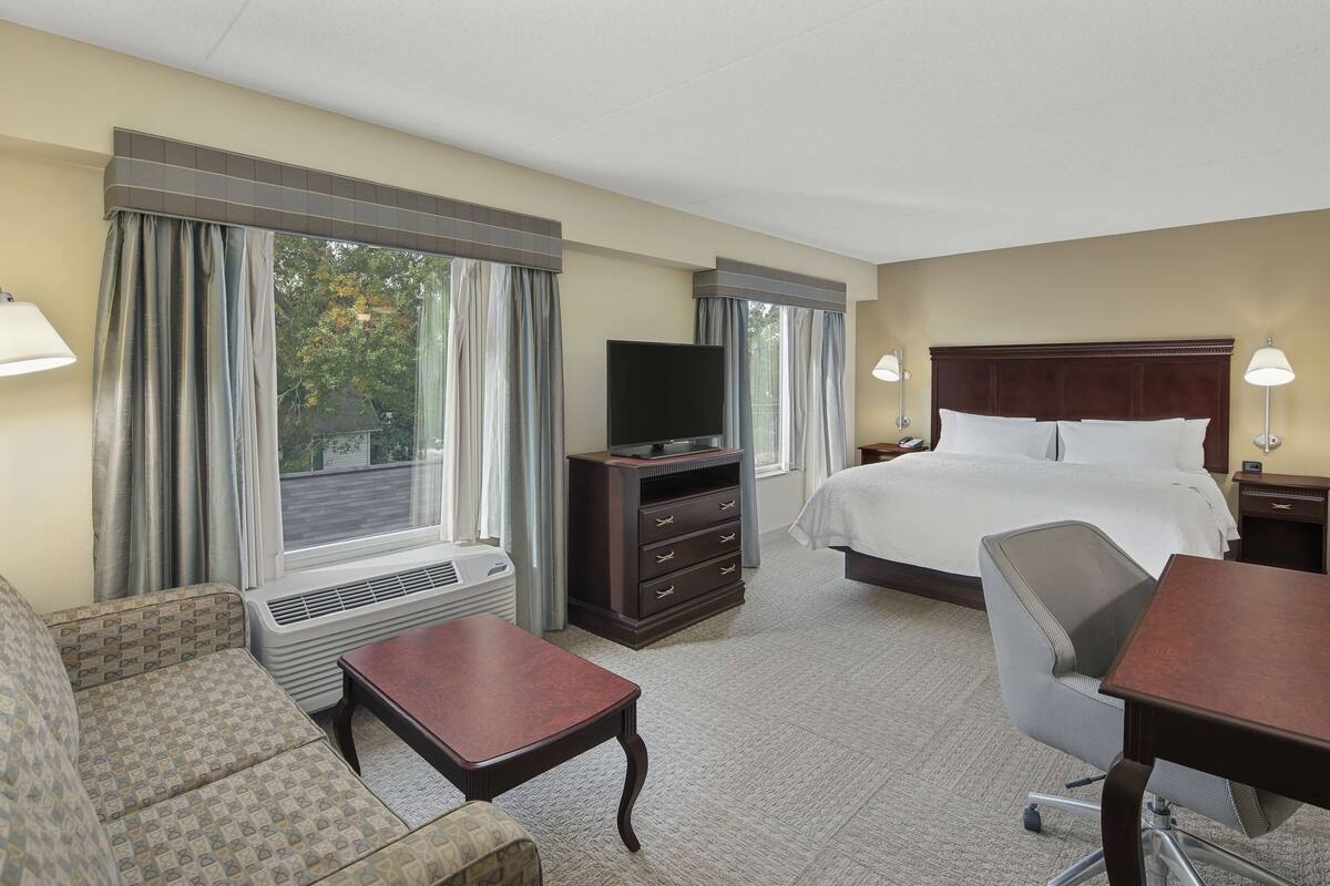 A hotel room with a bed, a TV, a desk, a chair, and a sofa.