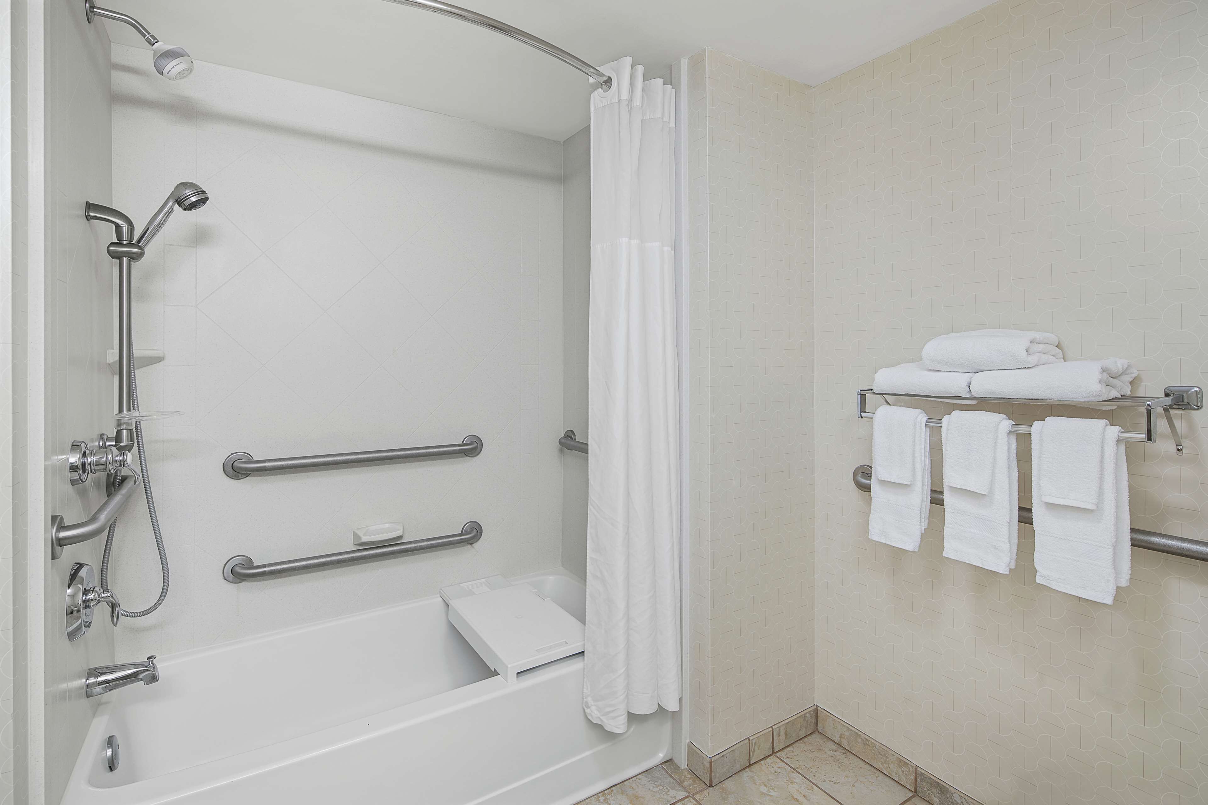A modern bathroom with a walk-in shower, grab bars, a towel rack, and a white tiled wall.