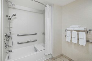 Ein modernes Badezimmer mit barrierefreier Dusche, Haltegriffen, einem Handtuchhalter und einer weißen Fliesenwand.