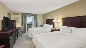 A hotel room with two beds, a desk with a chair, a television, and a window with curtains.