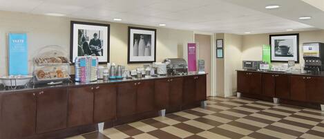 A check-in counter with a checkered floor, a coffee machine, and framed pictures on the wall.