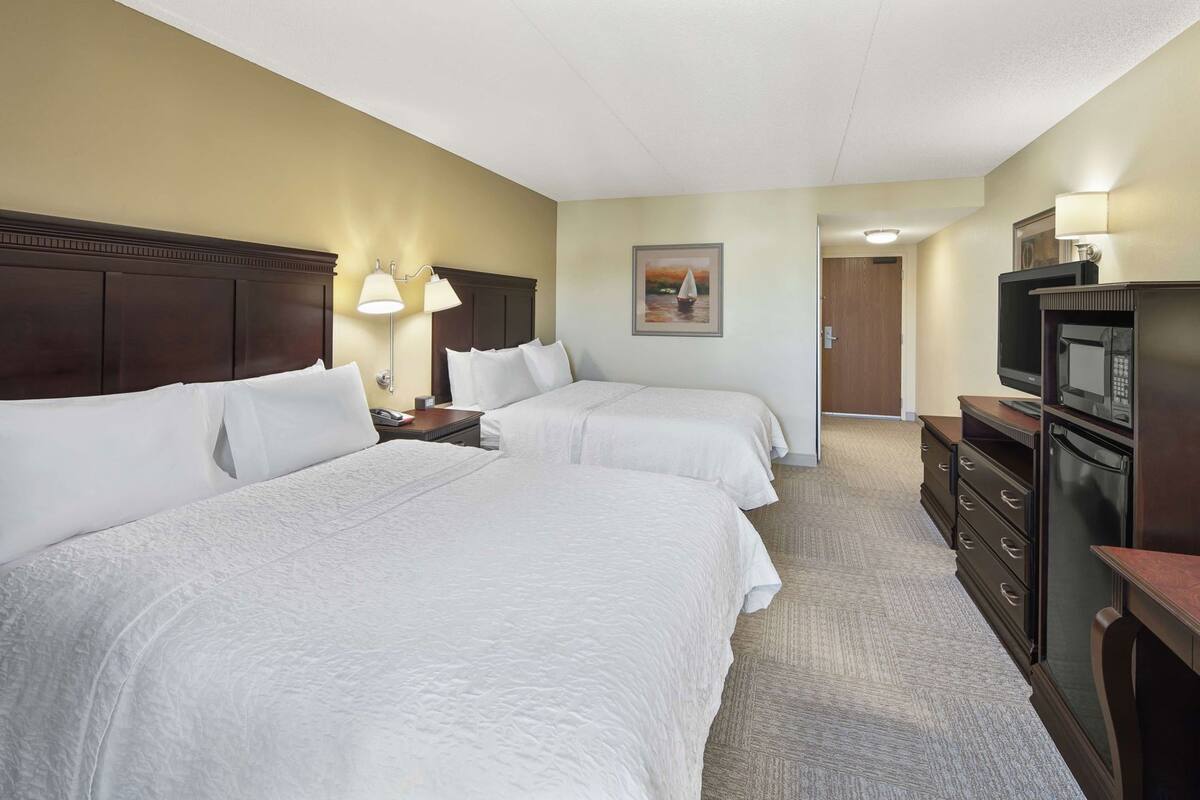 A hotel room with two beds, a TV, a refrigerator, and a painting on the wall.
