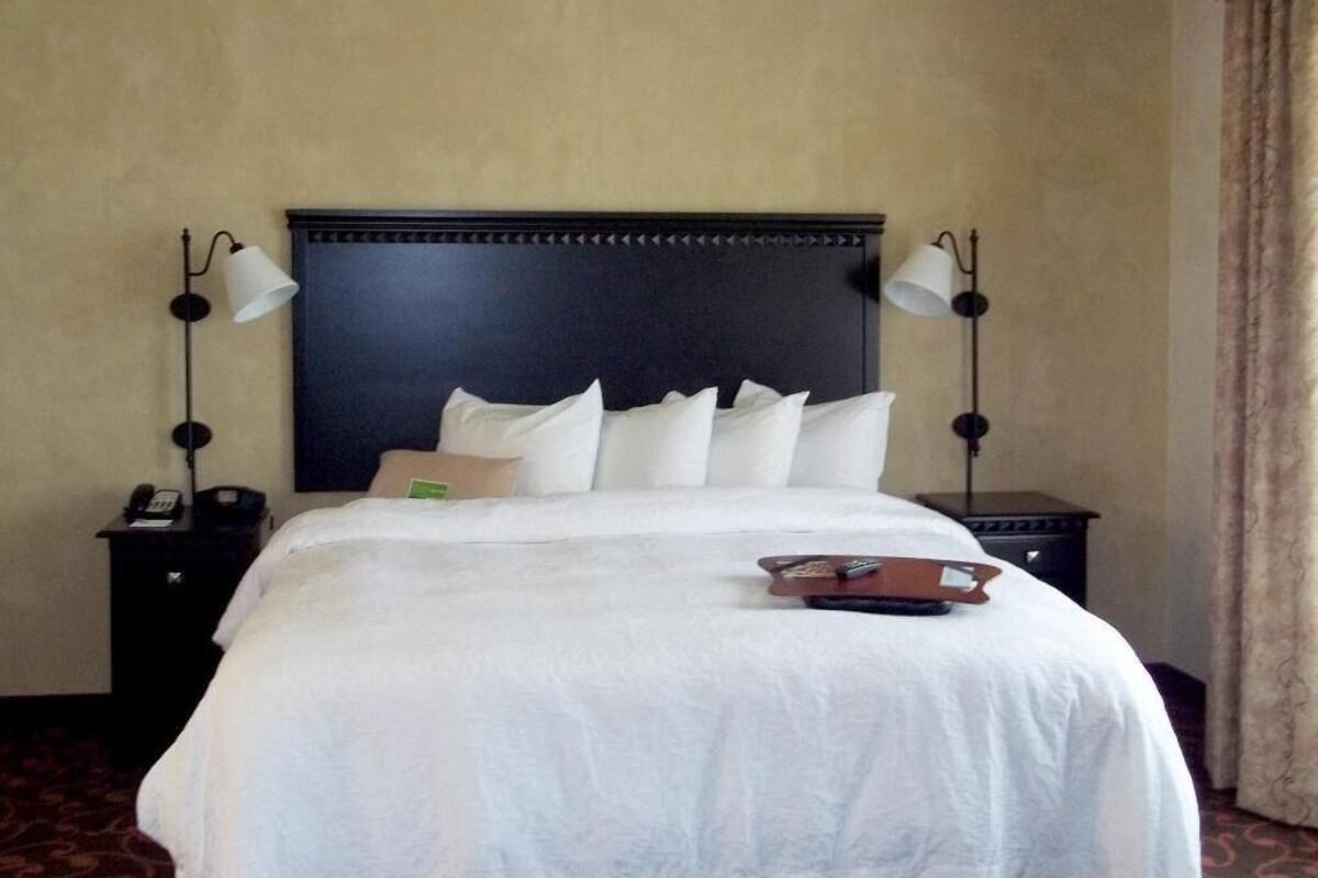 Une chambre d’hôtel avec un grand lit, deux lampes de chevet, une table de chevet avec un téléphone et une télécommande posée sur le lit.