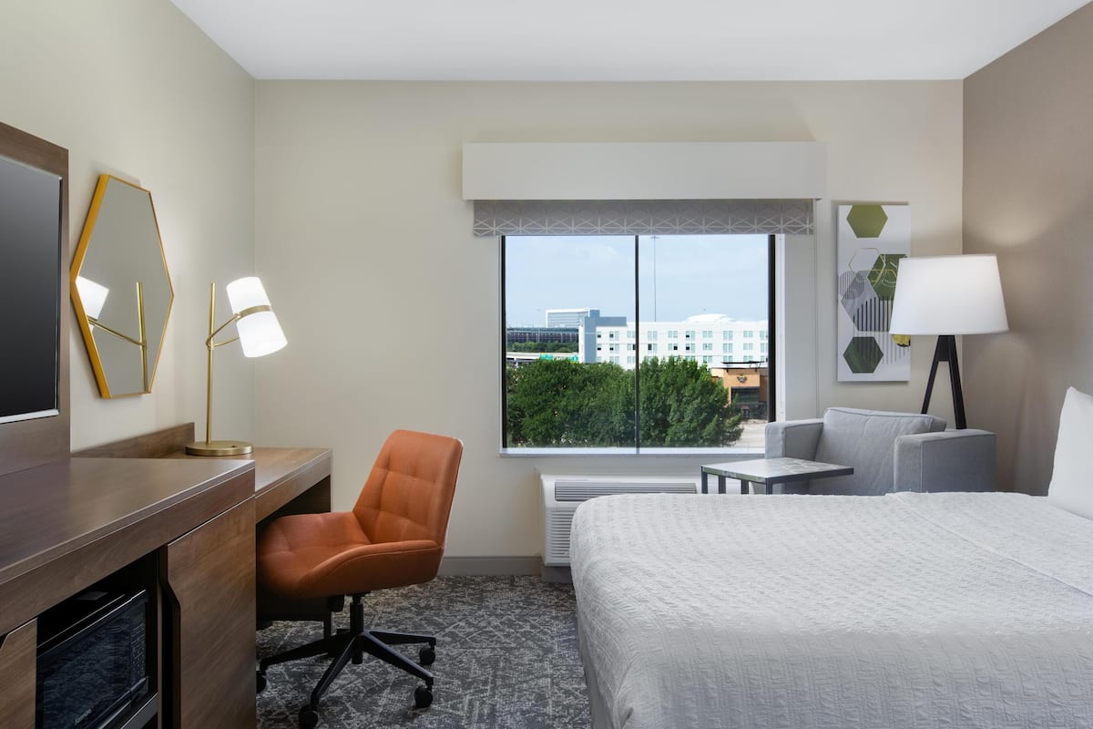 Une chambre d’hôtel équipée d’un lit, d’un bureau, d’une chaise et d’une grande fenêtre donnant sur la ville.