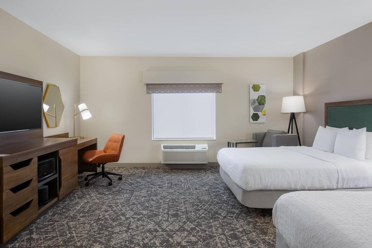 Une chambre d’hôtel équipée d’un lit, d’un bureau, d’une chaise, d’une télévision, d’un climatiseur et d’une fenêtre donnant sur un paysage agréable.