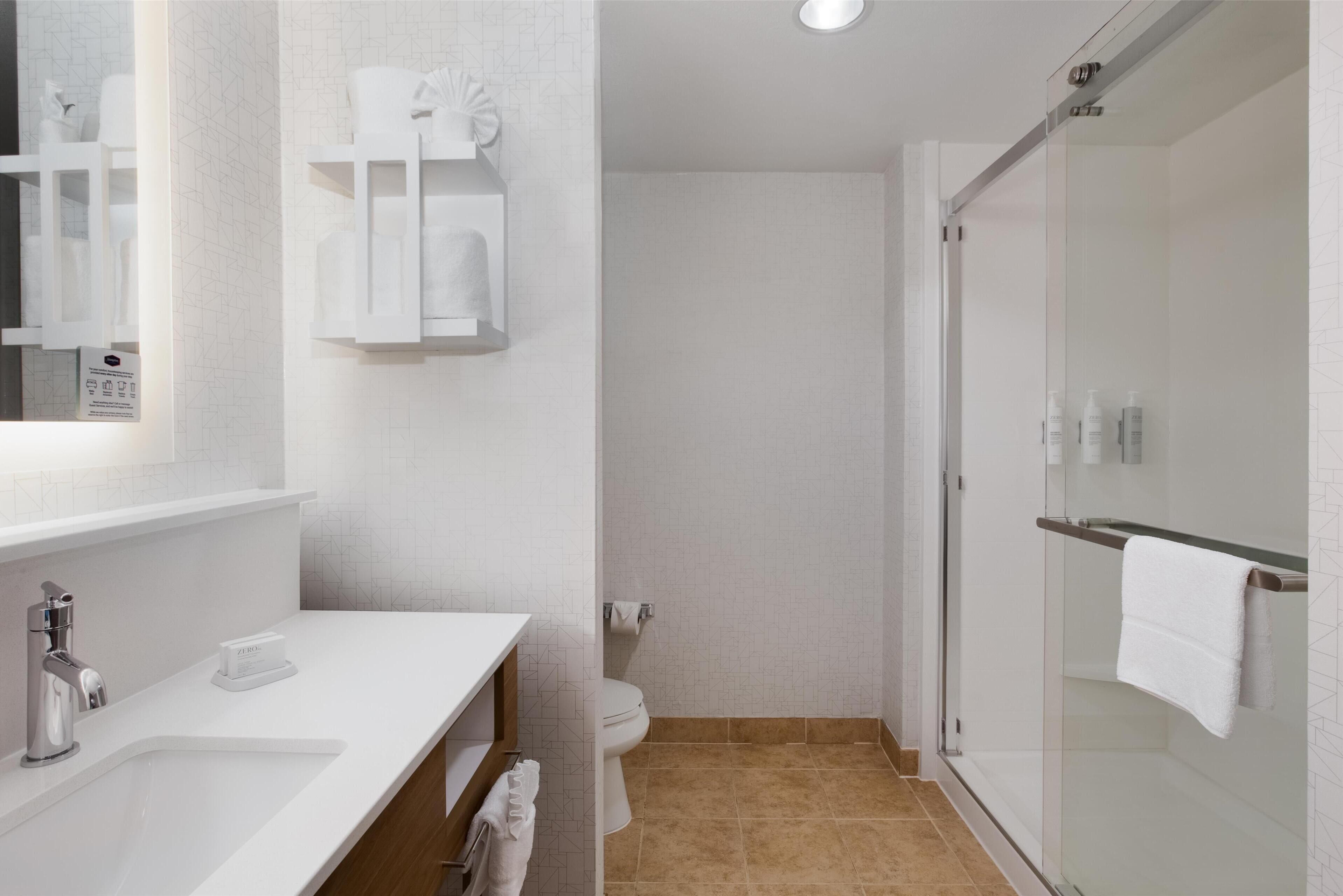 A modern bathroom with a white sink, mirror, and glass shower enclosure.