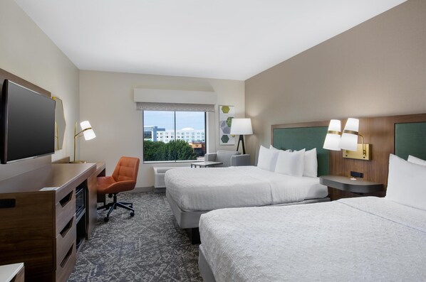 A hotel room with two beds, a desk, a chair, a TV, and a window with a city view.