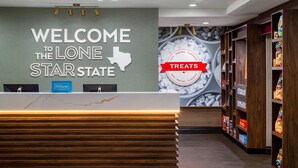 Ein Hotel-Rezeptionsbereich mit einem Schild, auf dem “Willkommen im Lone Star State” steht, einem “Hilton Honors”-Logo und einer Wand mit einem Schild, das “Snacks” anzeigt.