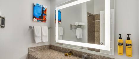 A bathroom with a granite countertop, a sink, a mirror, and two yellow toiletries bottles.