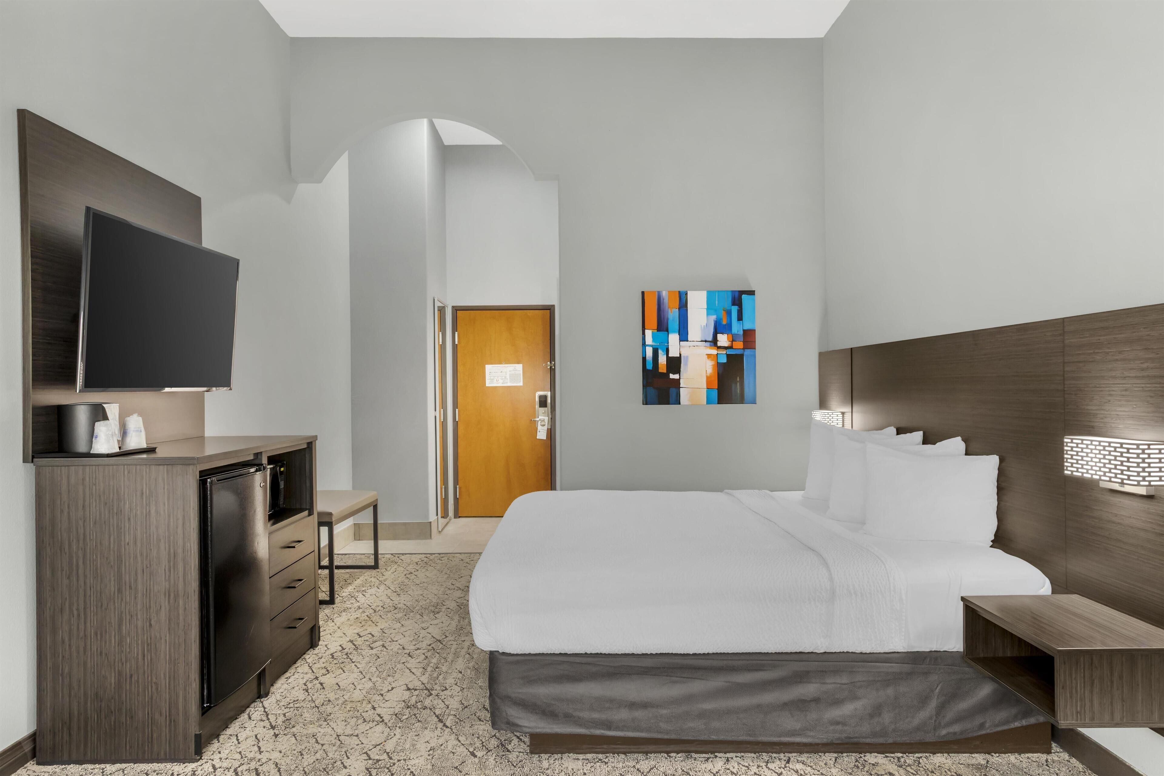 Una habitación de hotel con cama, televisión, escritorio y un cuadro en la pared.