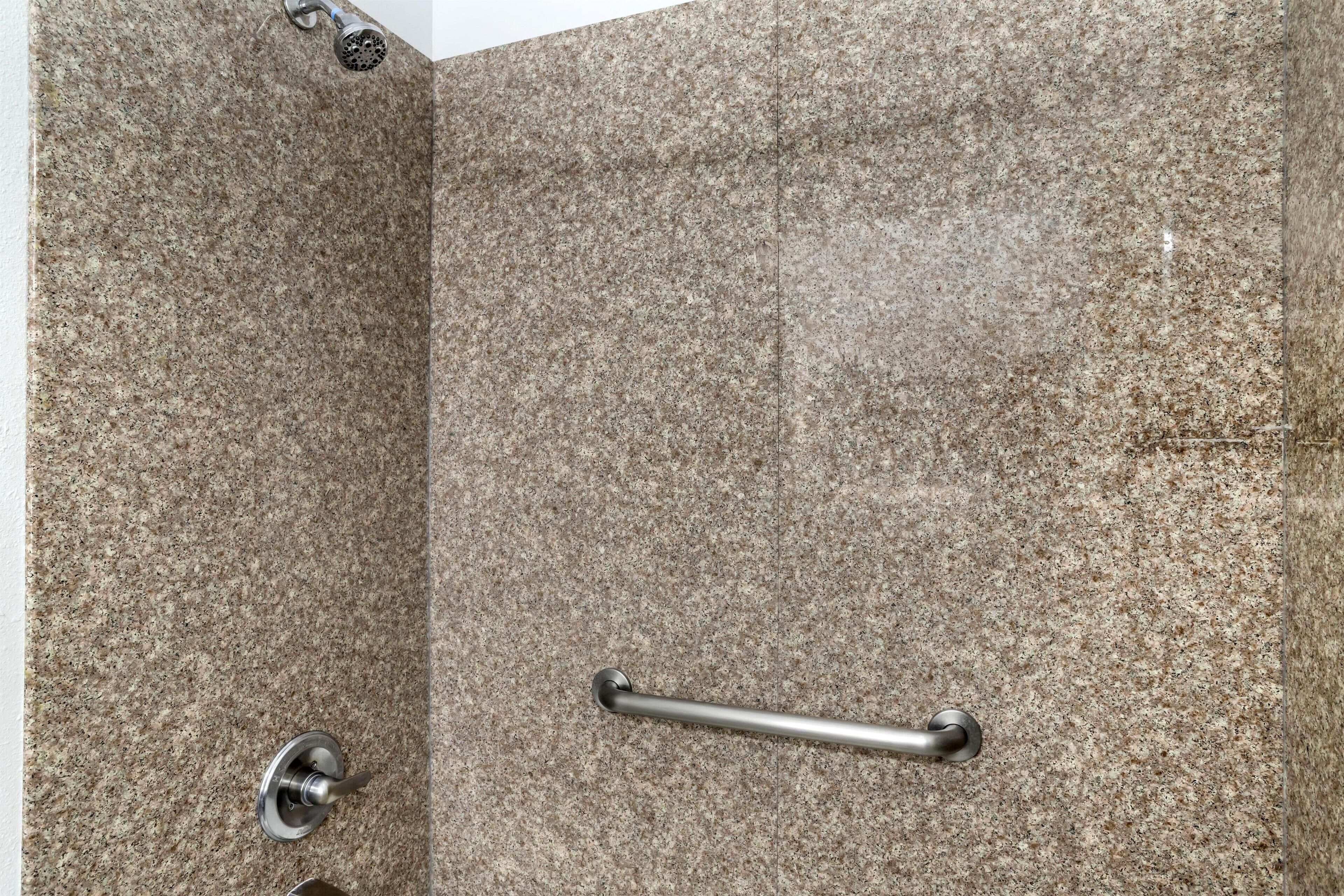 Un área de ducha con pared de granito, cabezal de ducha de mano y barra de apoyo.
