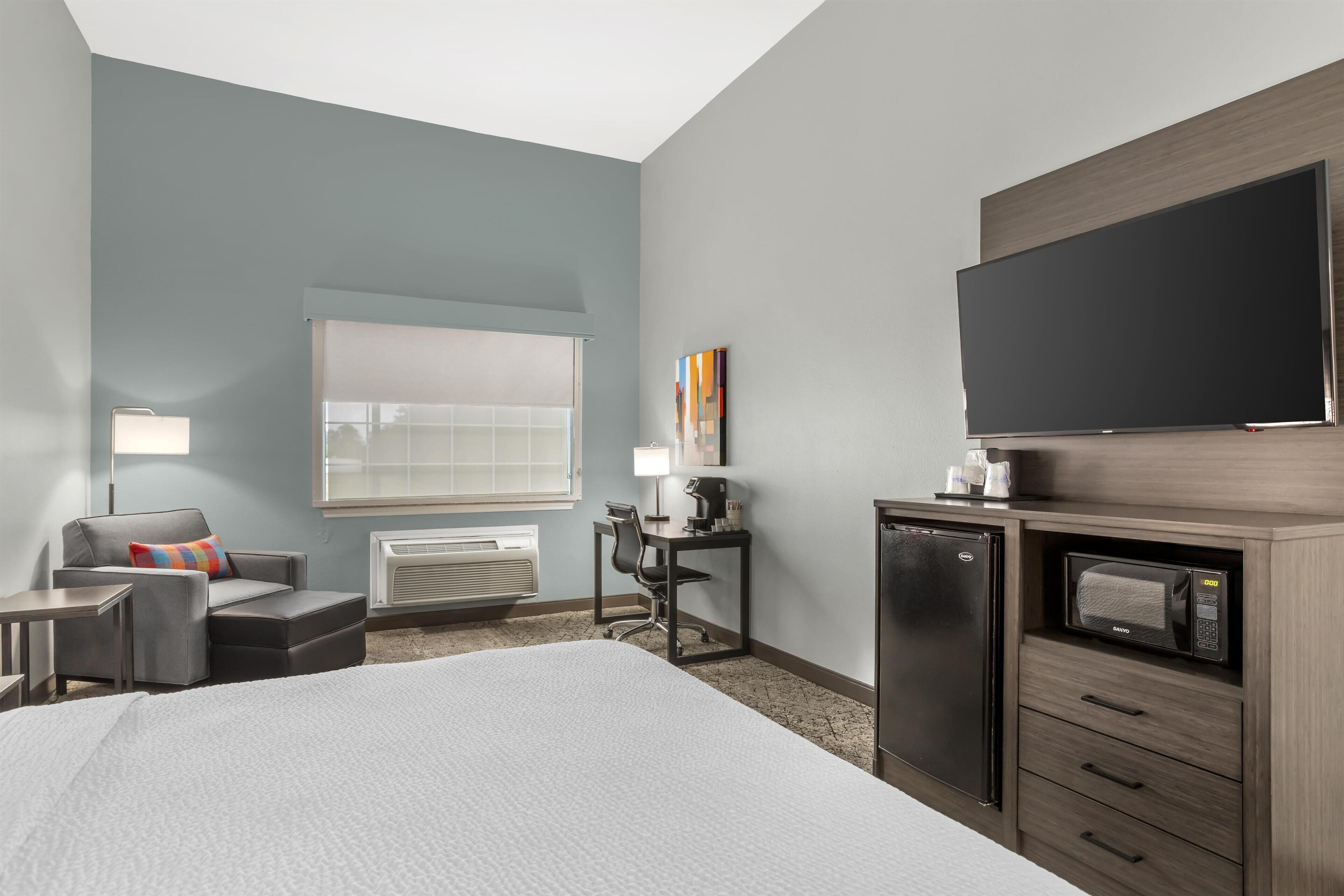 A hotel room with a bed, a desk with a chair, a television, a microwave, and a refrigerator.