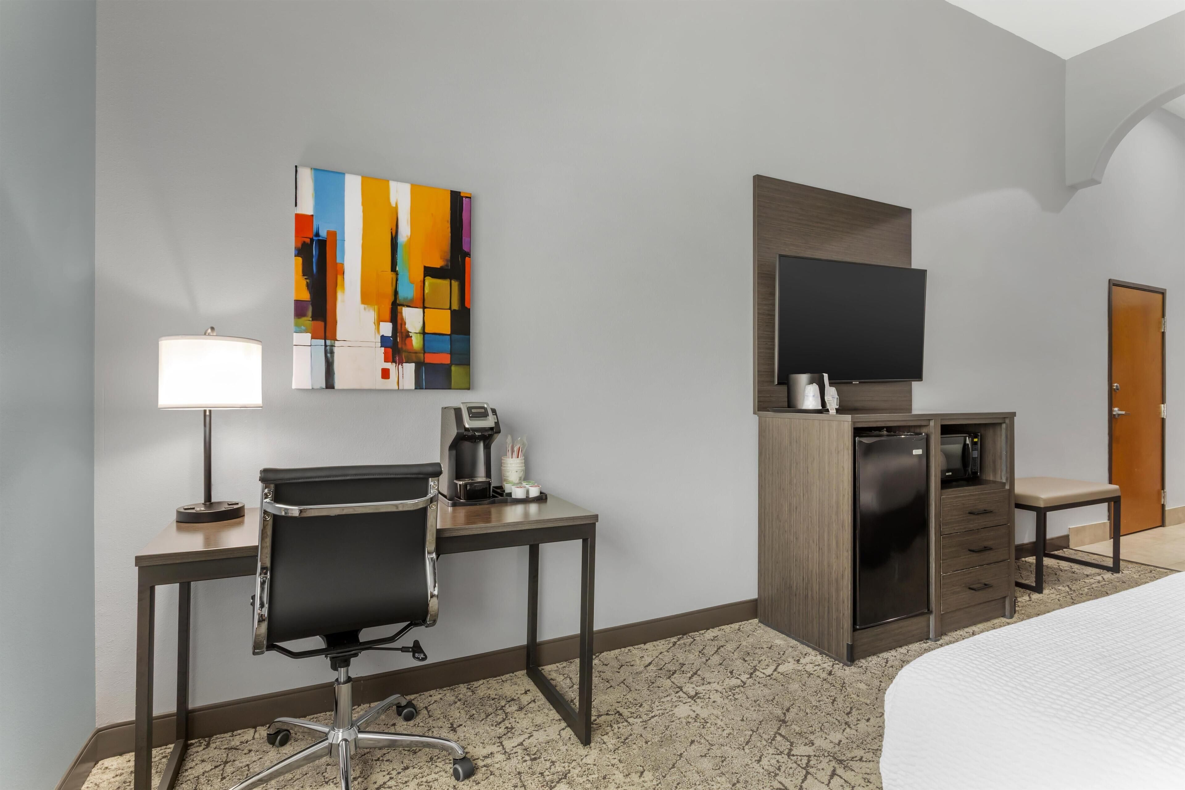 A hotel room with a desk, chair, television, minibar, and a bed.