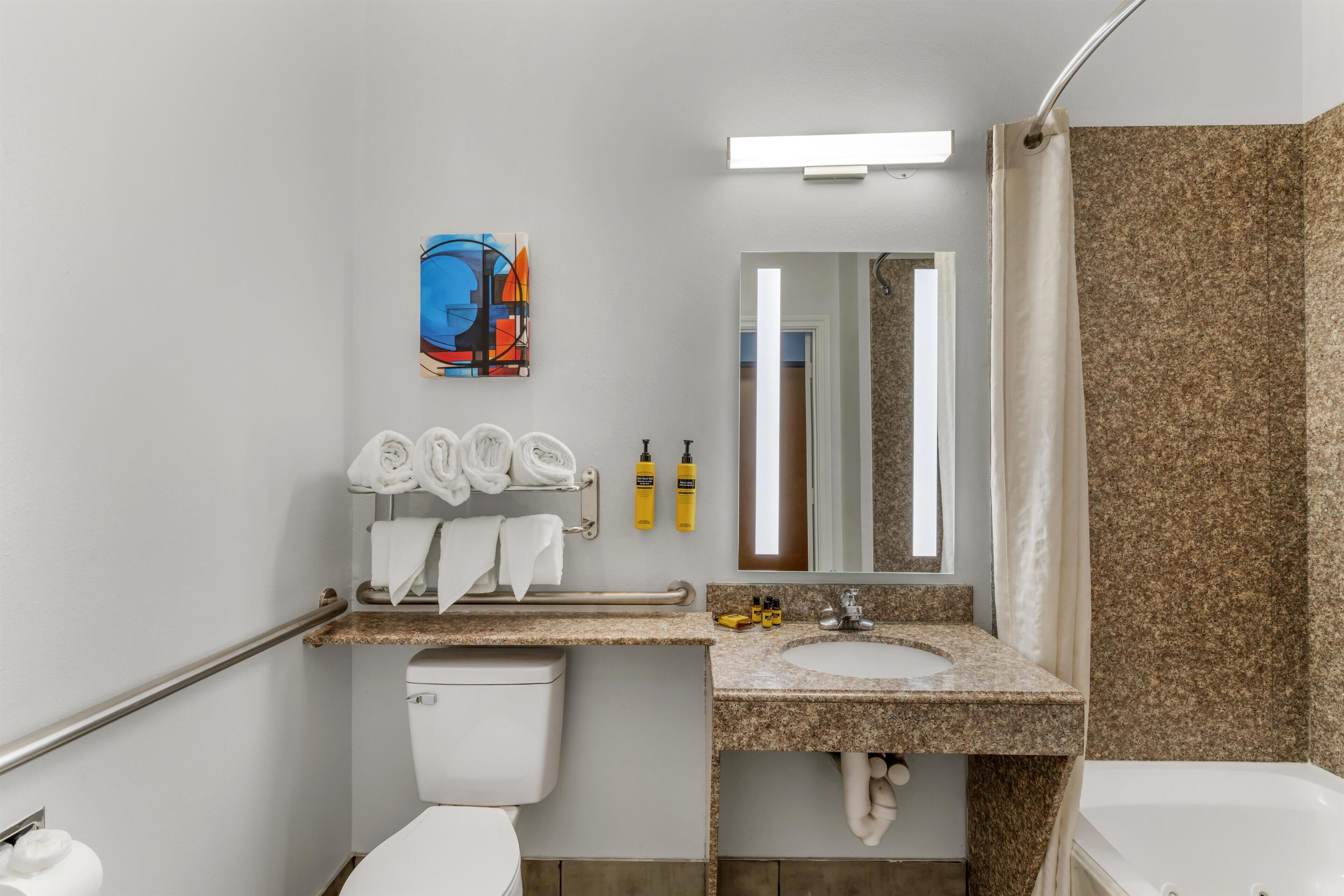 A modern bathroom with a toilet, sink, and shower. There is a towel rack with towels, a mirror, and a painting on the wall.