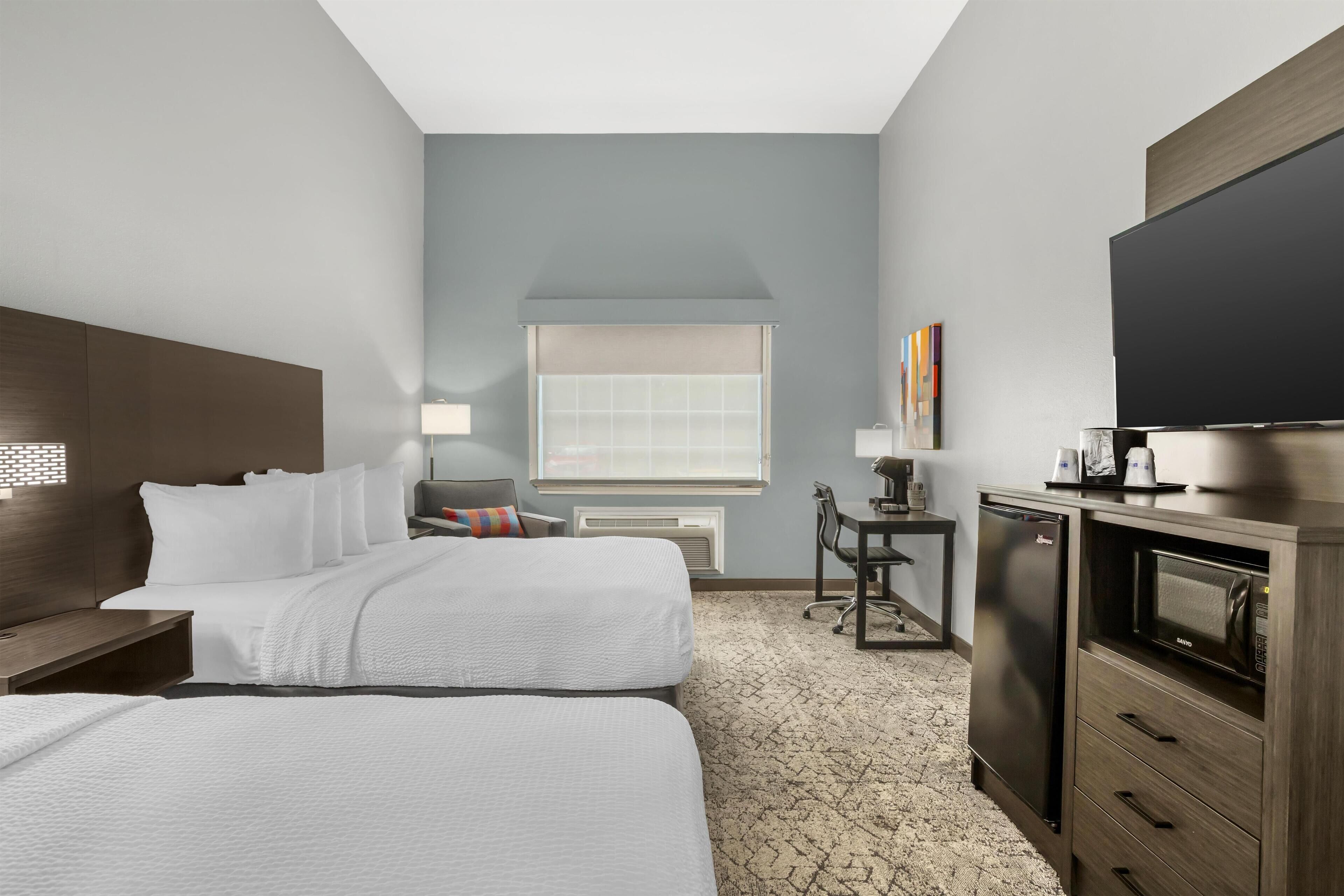 A hotel room with two beds, a desk, a television, and a microwave.