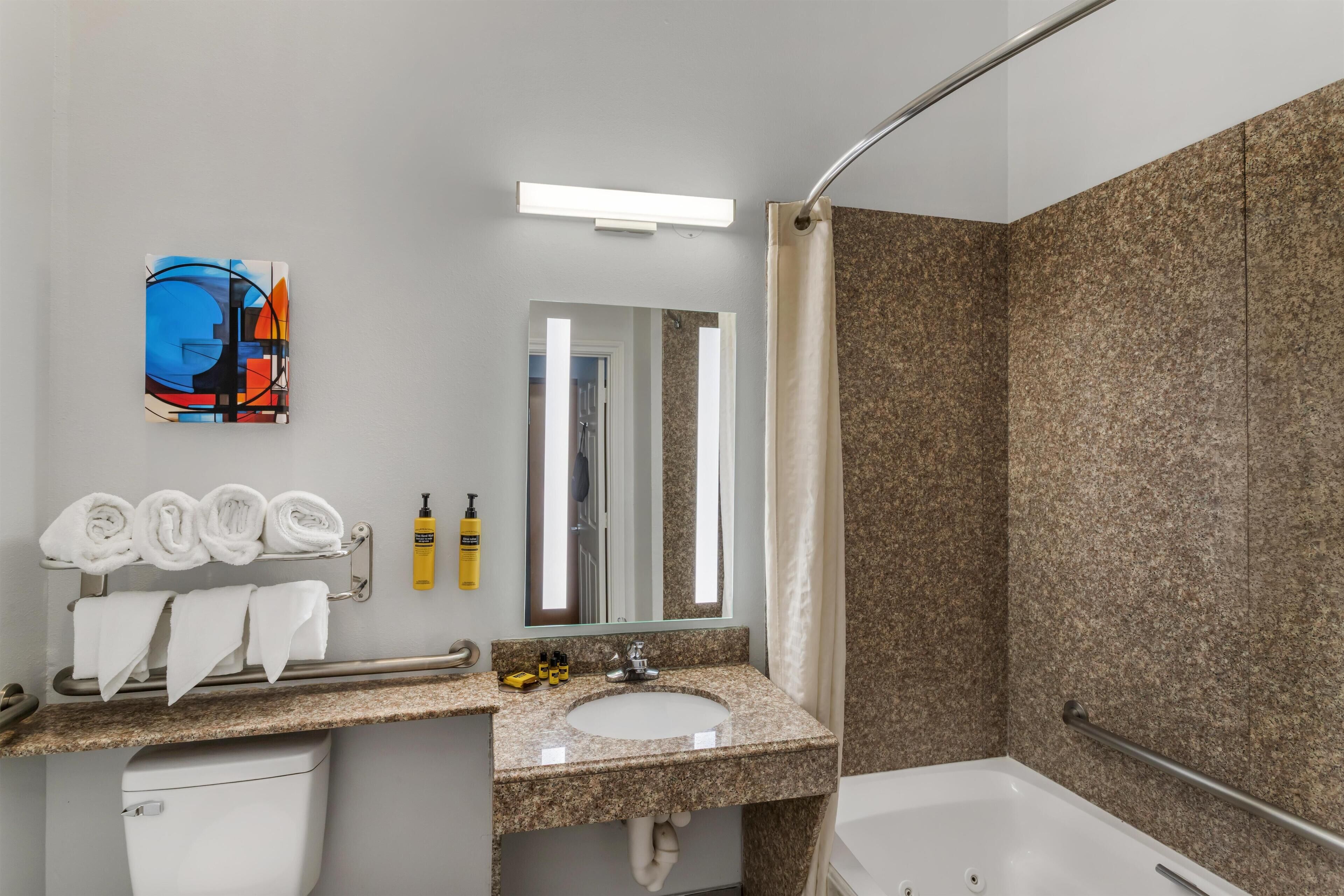 Un baño moderno con lavamanos de granito, inodoro blanco, ducha con puerta de cristal y toallero con toallas dobladas.