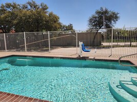 Una piscina transparente con una cerca de metal y una silla azul.