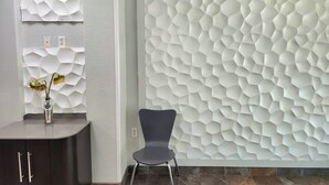 A modern interior with a hexagonal textured wall, a dark wooden cabinet, and a chair. - Baymont by Wyndham San Antonio Airport (San Antonio)