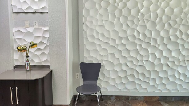 A modern interior with a hexagonal textured wall, a dark wooden cabinet, and a chair.