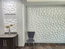 Un interior moderno con una pared hexagonal texturizada, un mueble de madera oscura y una silla.
