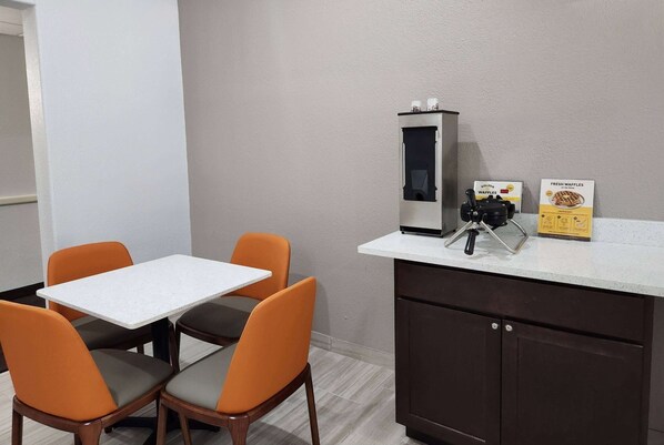 A small kitchenette with a coffee machine, a waffle maker, and a waffle box.