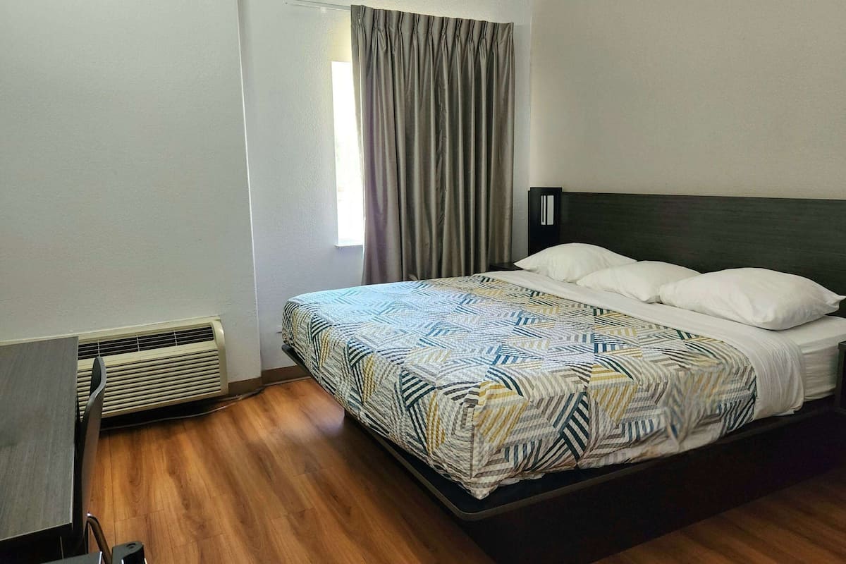 Une chambre d’hôtel avec un lit, un bureau et une fenêtre avec des rideaux.