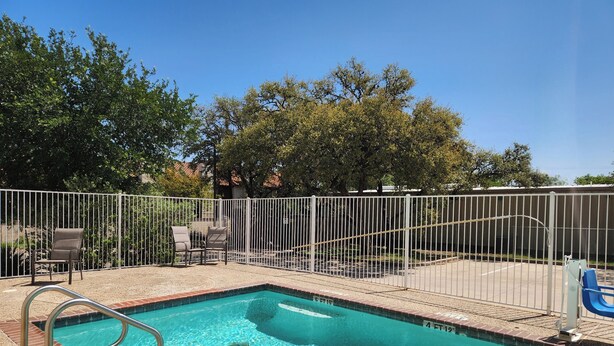 A swimming pool with a metal fence, lounge chairs, and a clear blue sky. - Baymont by Wyndham San Antonio Airport (San Antonio)