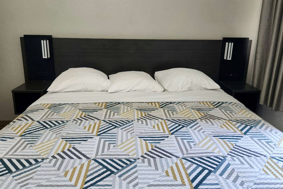 Un lit avec une couvre-lit à motifs géométriques, deux tables de chevet et une tête de lit sombre.