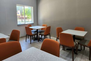 Un comedor con mesas y sillas, una ventana que ofrece vistas a zonas verdes y edificios, y un suelo de tonos claros.
