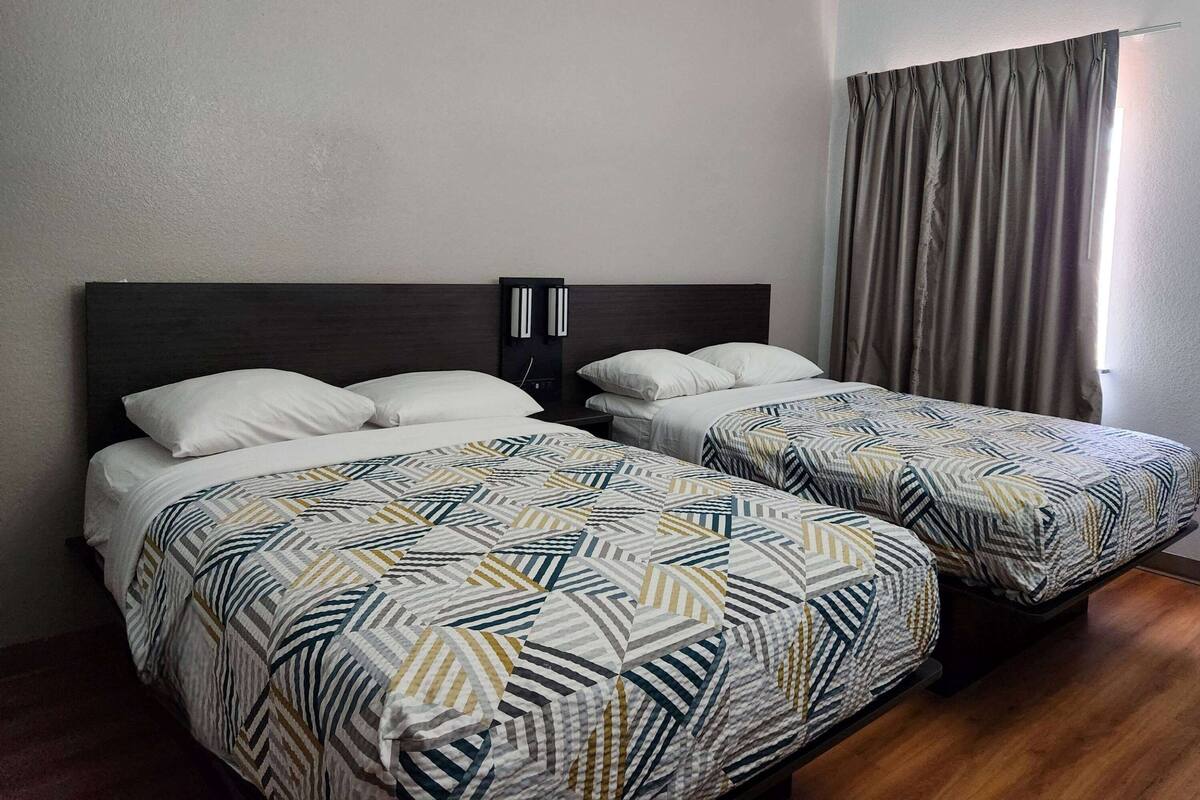 Une chambre d’hôtel avec deux lits, chacun agrémenté de draps à motifs et d’une tête de lit sombre.