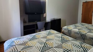 A hotel room with a bed, a desk with a chair, a TV mounted on the wall, and a door.