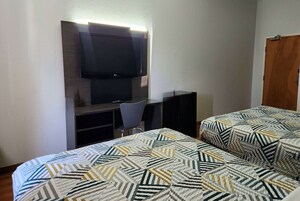 Una habitación de hotel con cama, escritorio con silla, televisor montado en la pared y una puerta.