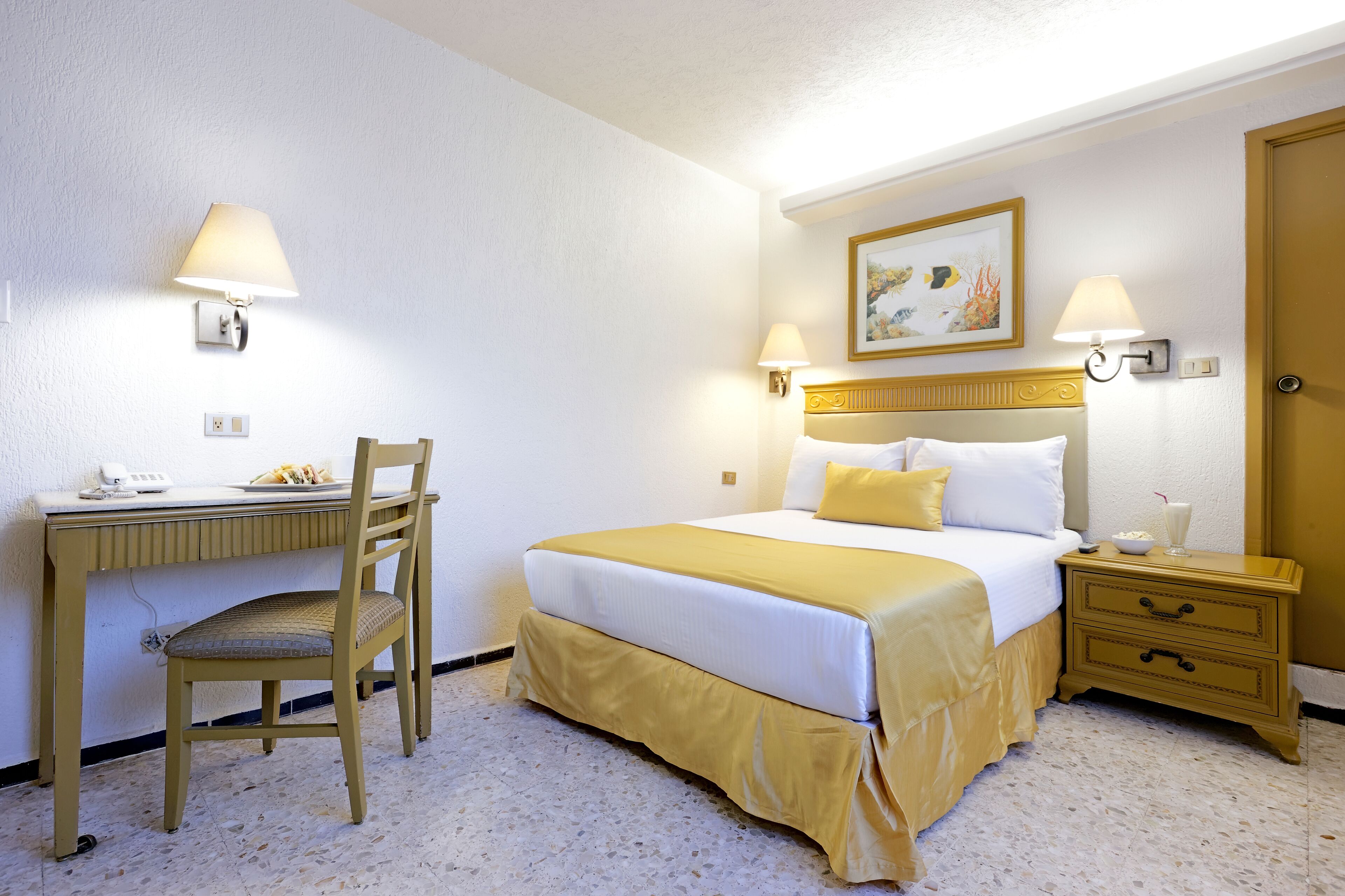 Ein Hotelzimmer mit Bett, Nachttisch, Lampe, Schreibtisch, Stuhl und einem Bild an der Wand.