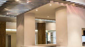 A modern reception area with a geometric ceiling design, a reception desk, and a visible hallway leading to other rooms.
