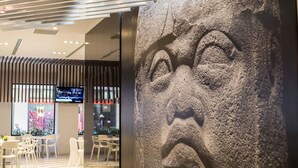 A modern interior with a large stone sculpture, a TV screen, and a seating area with chairs.