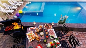 A poolside dining area with a grill, various food items, and lounge chairs.
