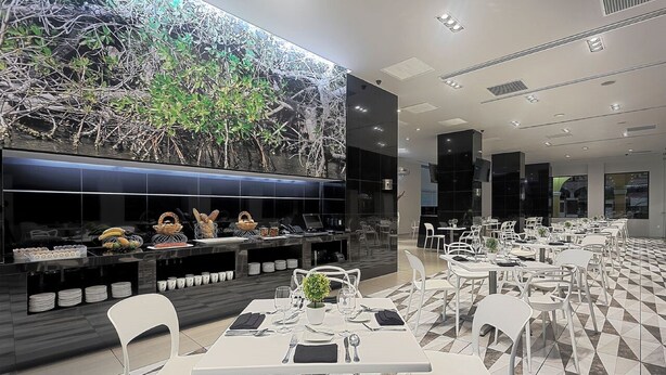 A modern restaurant with a high ceiling, a large digital display of a mangrove forest, and a tiled floor.