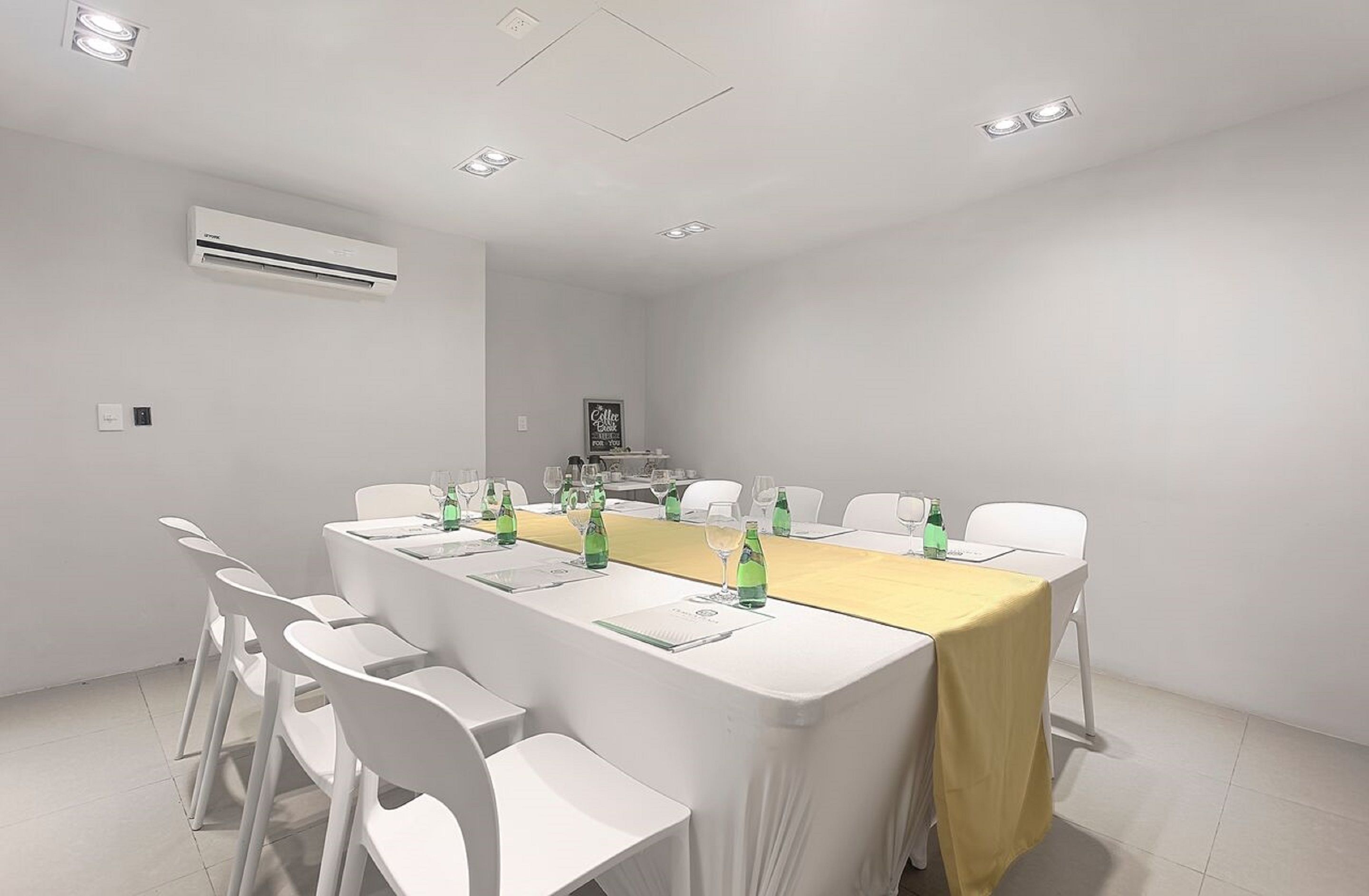 Una sala conferenze con un lungo tavolo, sedie bianche e una tovaglia gialla.