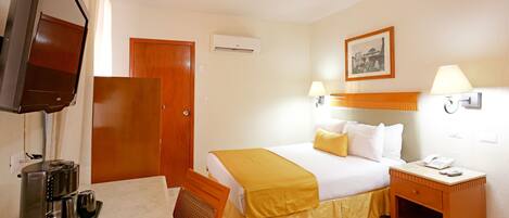 Habitación de hotel con cama, lámparas de noche, cafetera, televisor y puerta de madera.