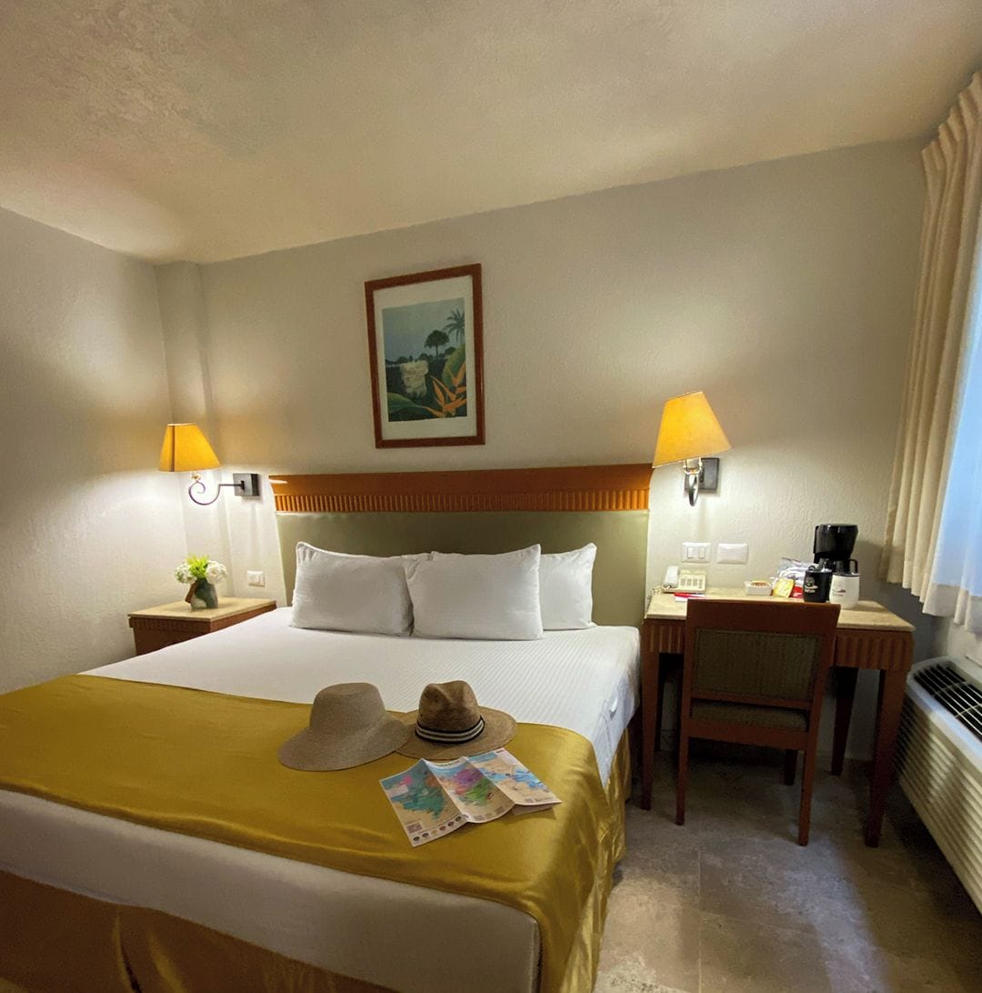 A hotel room with a bed, two bedside tables, a desk, a chair, and a picture on the wall.